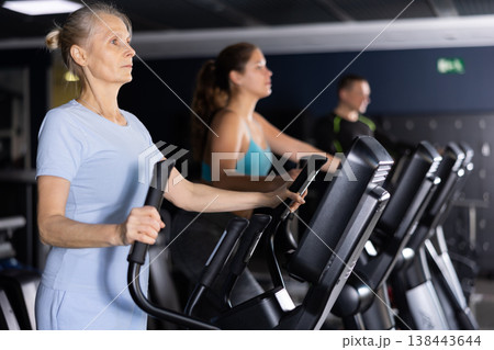 Elderly woman working out on elliptical machine in gym Elderly woman working out on elliptical machine in gym 138443644