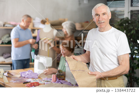 Elderly male participant present fabric billet, other people learn craft of tailor 138443722