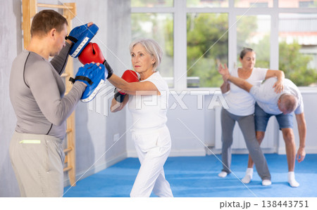 Old woman training boxing kicks on punch mitts held by instructor Old woman training boxing kicks on punch mitts held by instructor 138443751