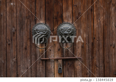 Traditional Chinese door knockers mounted on a weathered wooden door Traditional Chinese door knockers mounted on a weathered wooden door 138445819