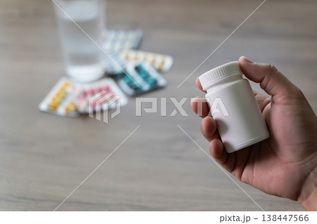 Close up of hand holding a white medicine pill bottle with blister packs and glass of water for healthcare treatment, showing professional pharmacy medication and a beautiful wellness concept 138447566