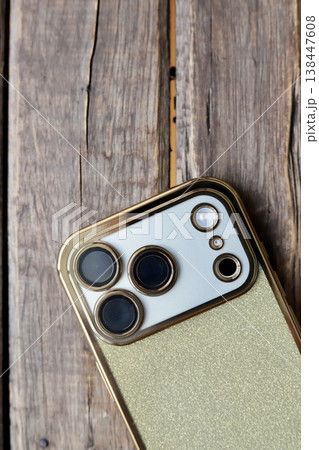 ゴールドラメの背面ケースをつけた3眼カメラのスマートフォン 138447608