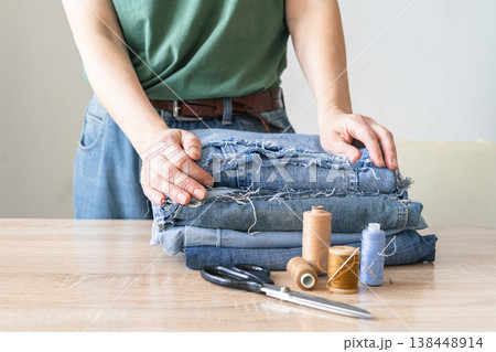 Person preparing upcycled denim fabric, thread, and scissors for sewing. Creative craft hobby saving the environment, upcycling denim jeans reusing old clothes. Reusing things 138448914