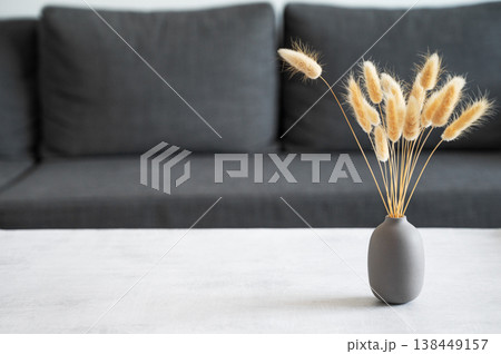 A bouquet of dried herbs in a gray vase on a light textured table against a gray sofa. A bouquet of dried herbs in a gray vase on a light textured table against a gray sofa. 138449157