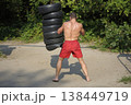 Muscular boxer training outdoors hitting heavy punching bag made of car tires in the park 138449719