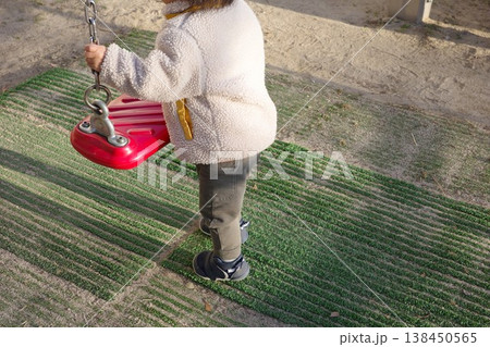 公園でブランコの鎖を握って遊ぶ冬服の子供 138450565
