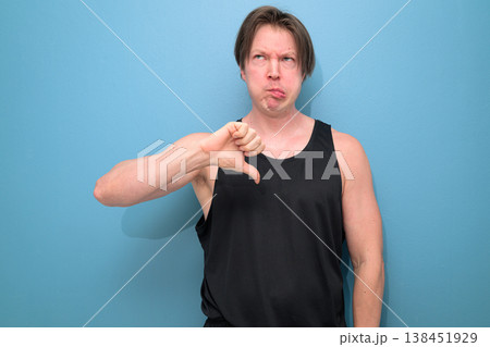 Caucasian Man Giving Thumbs Down and Making Silly Face on Blue Background Caucasian Man Giving Thumbs Down and Making Silly Face on Blue Background 138451929
