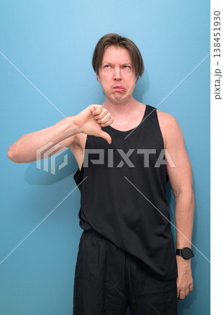 Scandinavian Man Giving Thumbs Down and Making Silly Face on Blue Background Scandinavian Man Giving Thumbs Down and Making Silly Face on Blue Background 138451930