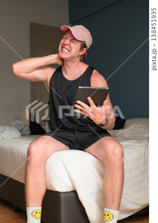 Caucasian Man with Neck Pain Holding Tablet on Bed in Minimalist Bedroom 138451935