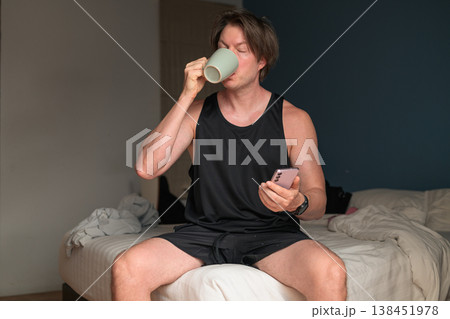 Man Drinking Coffee and Using Smartphone on Bed in Minimalist Bedroom Man Drinking Coffee and Using Smartphone on Bed in Minimalist Bedroom 138451978