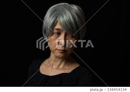 黒背景の前で恨めしい視線を送る白髪のシニア女性 138454134