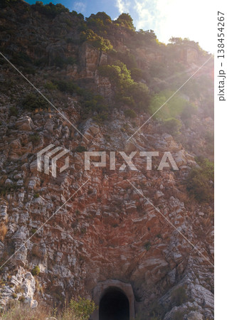 Close up of bright orange coastal rocks in Petrovac with stone path tourists and cliff tunnel with green trees showing nature and travel scene Close up of bright orange coastal rocks in Petrovac with stone path tourists and cliff tunnel with green trees showing nature and travel scene 138454267