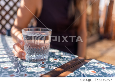 Woman Holding Glass of Water at Outdoor Cafe Table. Refreshment and Hydration Concept 138459297