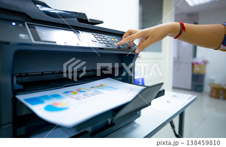 Office worker prints paper on multifunction laser printer. Copy, print, scan, and fax machine in office. Document and paper work. Print technology. Hand press on photocopy machine. Scanner equipment. 138459810