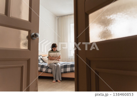 An adult woman feeling sad, lonely, and depressed while sitting on her bed, embracing a pillow in a solitary moment at home 138460853
