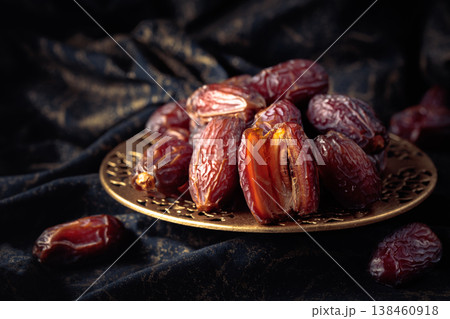Dates fruits in a golden bowl on black fabric with gold ornamentation. Dates fruits in a golden bowl on black fabric with gold ornamentation. 138460918