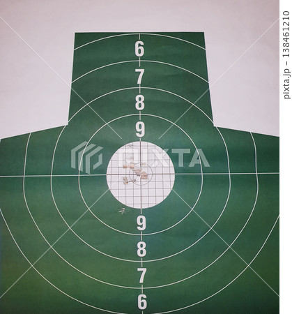 Close-up of a green paper shooting target with multiple bullet holes in the white bullseye center. Concept of high precision, expert marksmanship, and goal achievement. Close-up of a green paper shooting target with multiple bullet holes in the white bullseye center. Concept of high precision, expert marksmanship, and goal achievement. 138461210
