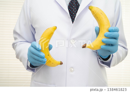 Male doctor stands holding a banana, penis health. Male doctor stands holding a banana, penis health. 138461823