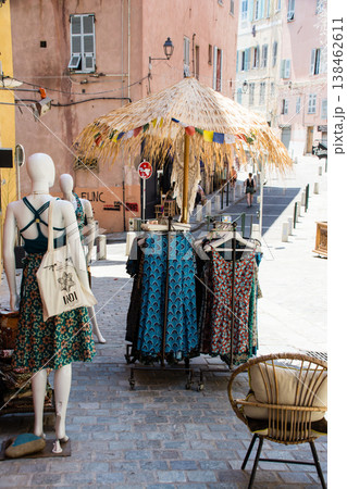 明るい日差しの下の店先に置かれた麦わらのパラソルと洋服 地中海に浮かぶフランス領のコルシカ島にて 明るい日差しの下の店先に置かれた麦わらのパラソルと洋服 地中海に浮かぶフランス領のコルシカ島にて 138462611