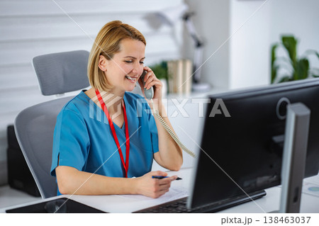 Female healthcare worker talking on phone at clinic reception desk 138463037