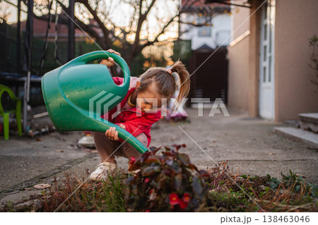 Little girl watering plants with green watering can in yard Little girl watering plants with green watering can in yard 138463046