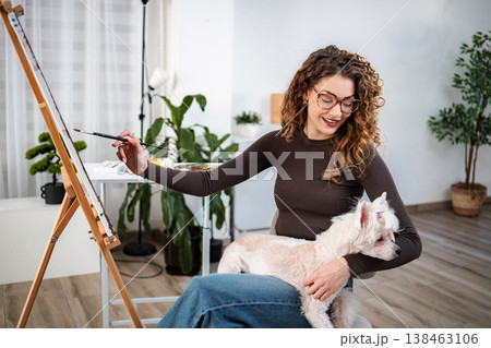 Woman artist painting at easel with dog in home studio 138463106
