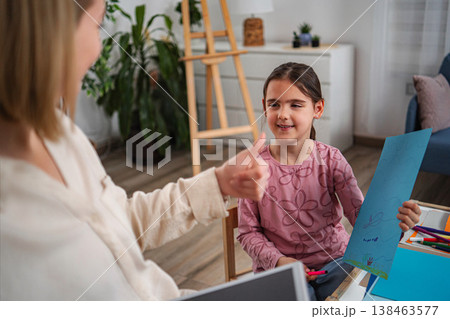 Child smiling showing artwork while therapist gives a thumbs up 138463577