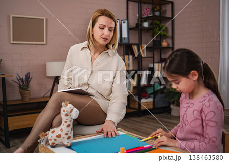 Psychologist observing young girl drawing during child therapy session 138463580