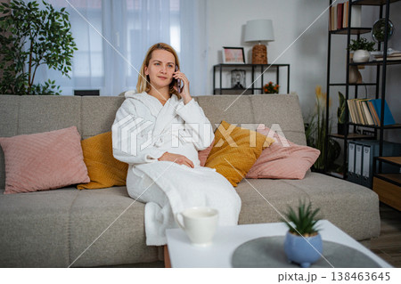 Woman talking on smartphone in bathrobe relaxing on couch at home 138463645