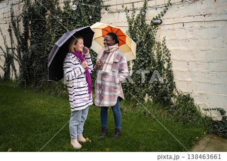 Two diverse friends communicating outdoors on rainy autumn day 138463661