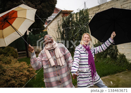 Happy adult women friends laughing playing in rain with umbrellas Happy adult women friends laughing playing in rain with umbrellas 138463671