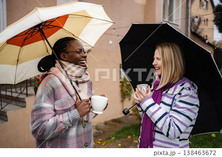 Multi-ethnic women friends laughing and drinking coffee in rain Multi-ethnic women friends laughing and drinking coffee in rain 138463672