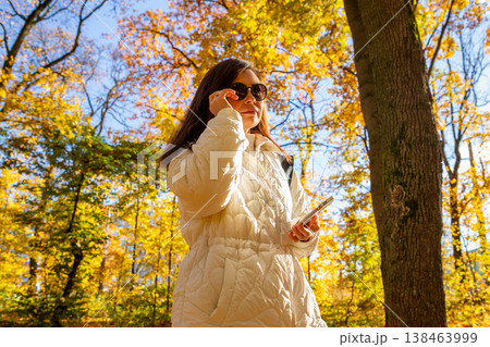 Successful woman in autumn forest talking on smartphone. Mature businesswoman or blogger enjoying nature in park. Concept of lifestyle, freedom, mobile communication and work balance. Successful woman in autumn forest talking on smartphone. Mature businesswoman or blogger enjoying nature in park. Concept of lifestyle, freedom, mobile communication and work balance. 138463999