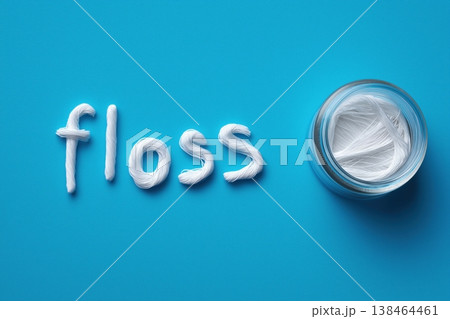 Sparkling white floss spelling 'floss' next to a clean jar of dental thread on blue Sparkling white floss spelling 'floss' next to a clean jar of dental thread on blue 138464461