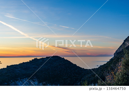 Serene Sunset Over Coastal Hills And Calm Sea With Sky Contrails At Dusk Serene Sunset Over Coastal Hills And Calm Sea With Sky Contrails At Dusk 138464750
