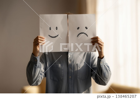 Person expressing mood swings using happy and sad face drawings held in front of face for mental health awareness. Person expressing mood swings using happy and sad face drawings held in front of face for mental health awareness. 138465207