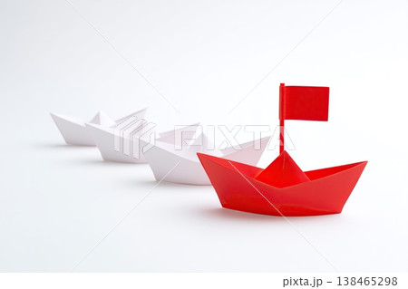 Red paper boat leading a fleet of white origami boats, symbolizing leadership and direction in a business or strategic context. 138465298