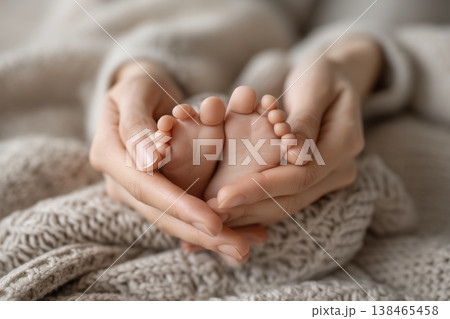 Tender moment as a mother gently cradles her newborn baby's delicate feet with love and care on soft blanket. 138465458