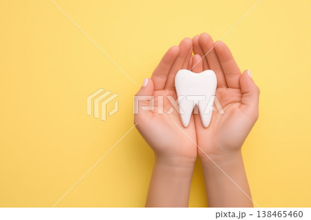 Woman gently holds a healthy white tooth model, promoting dental care and oral hygiene on a vibrant yellow backdrop. Woman gently holds a healthy white tooth model, promoting dental care and oral hygiene on a vibrant yellow backdrop. 138465460