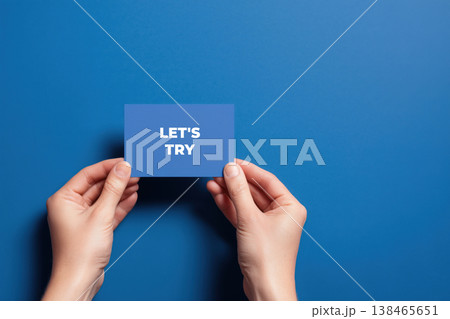 Hands holding a card with the phrase Let's Try on a blue background for inspiration, motivation, and positive thinking. 138465651