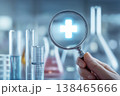 Magnifying health, a hand holds a magnifying glass over a glowing plus sign in a laboratory setting. 138465666