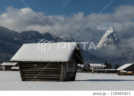Wooden barn with snowy roof and striking alpine mountain in Bavarian winter landscape 138465821