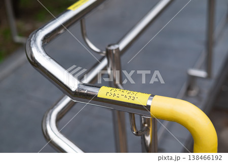 Stainless steel handrail with braille markings and yellow safety coating, accessibility infrastructure outdoors Stainless steel handrail with braille markings and yellow safety coating, accessibility infrastructure outdoors 138466192