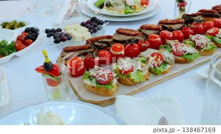 Gourmet appetizer platter featuring miniature sandwiches layered with tomatoes, meat, cheese, lettuce, olives, sundried tomatoes on rustic wooden serving board 138467169