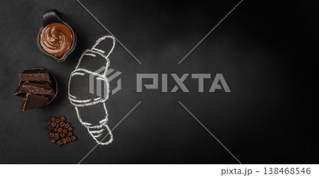 Chocolate spread, dark chocolate and coffee beans with croissant chalk drawing on black background, top view Chocolate spread, dark chocolate and coffee beans with croissant chalk drawing on black background, top view 138468546