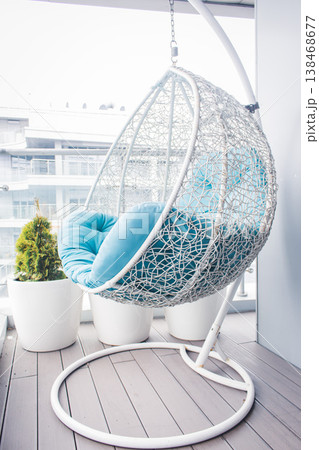 Cozy modern apartment concept. Cozy wicker hammock on balcony. Hanging chair with a blue pillow on wooden terrace. Luxury house design. Dream house decoration. Comfortable home with modern furniture. Cozy modern apartment concept. Cozy wicker hammock on balcony. Hanging chair with a blue pillow on wooden terrace. Luxury house design. Dream house decoration. Comfortable home with modern furniture. 138468677