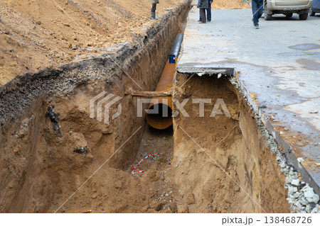 Construction workers lay a large water pipe under the road. Repair repair of city water supply in a deep trench on a city street. Improving the quality of life, reconstruction 138468726