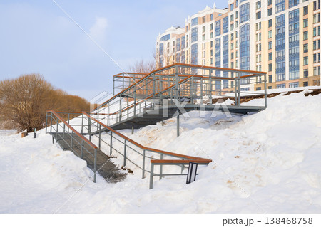 Snow covered hillside with winding metal ramps for wheelchairs and for baby carriages for accessibility in urban setting Snow covered hillside with winding metal ramps for wheelchairs and for baby carriages for accessibility in urban setting 138468758