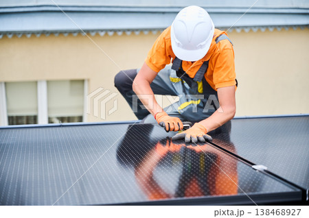 Worker building photovoltaic solar panel system on rooftop of house. Man engineer in helmets and gloves installing solar module with help of hex key outdoors. Renewable energy generation concept. Worker building photovoltaic solar panel system on rooftop of house. Man engineer in helmets and gloves installing solar module with help of hex key outdoors. Renewable energy generation concept. 138468927