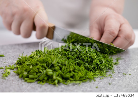 A woman's hands chop dill on a gray board 138469034
